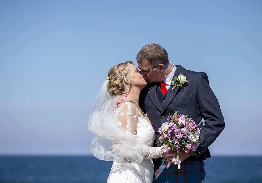 Bride and groom kiss with sea in background